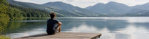 Einzelcoaching für Führungskräfte zur Persönlichkeits- und Potenzialentwicklung: junger Mann sitzt auf einem Steg am See mit Blick auf Berge