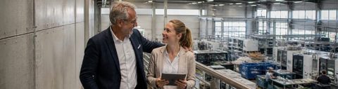 Nachfolge-Coaching für Führungskräfte: älterer Mann begleitet junge Frau durch eine Maschinenhalle in der Produktion